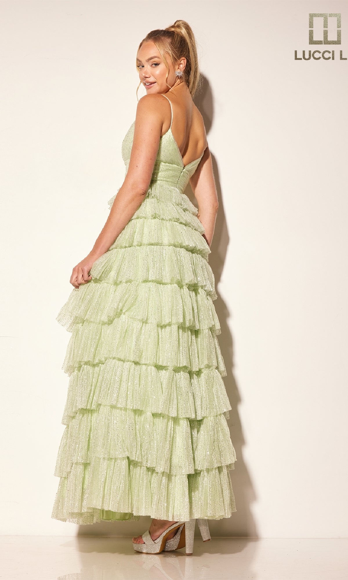 Woman poses sideways against a plain white background, wearing the Lucci Lu 1342 Glitter Tulle Ruffle Prom Dress in light green, featuring a tiered ruffle skirt and sparkling tulle fabric.
